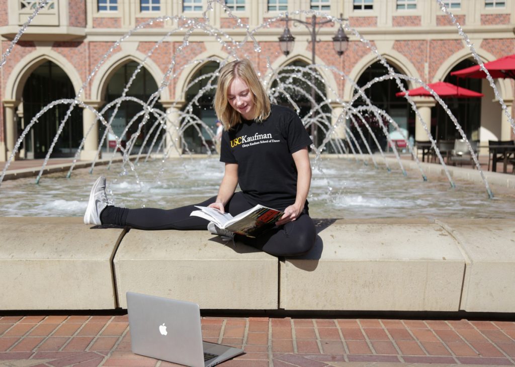 Girl sitting outside studying in front of fountain.