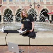 Girl sitting outside studying in front of fountain.