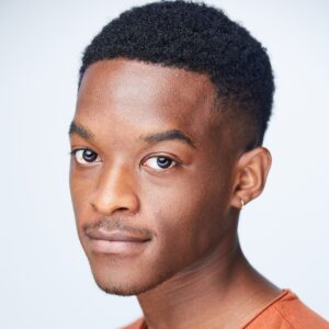 close up of a guy with short dark hair wearing an orange shirt