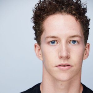 close up of a guy with short brown curly hair and blue eyes wearing a black shirt