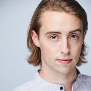 close up of a guy with medium length blonde hair wearing a white button up