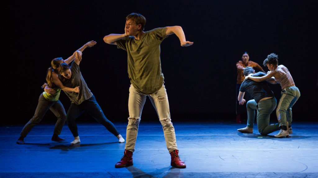 Dancer with hand on cheek in front of two clumps of dancers onstage