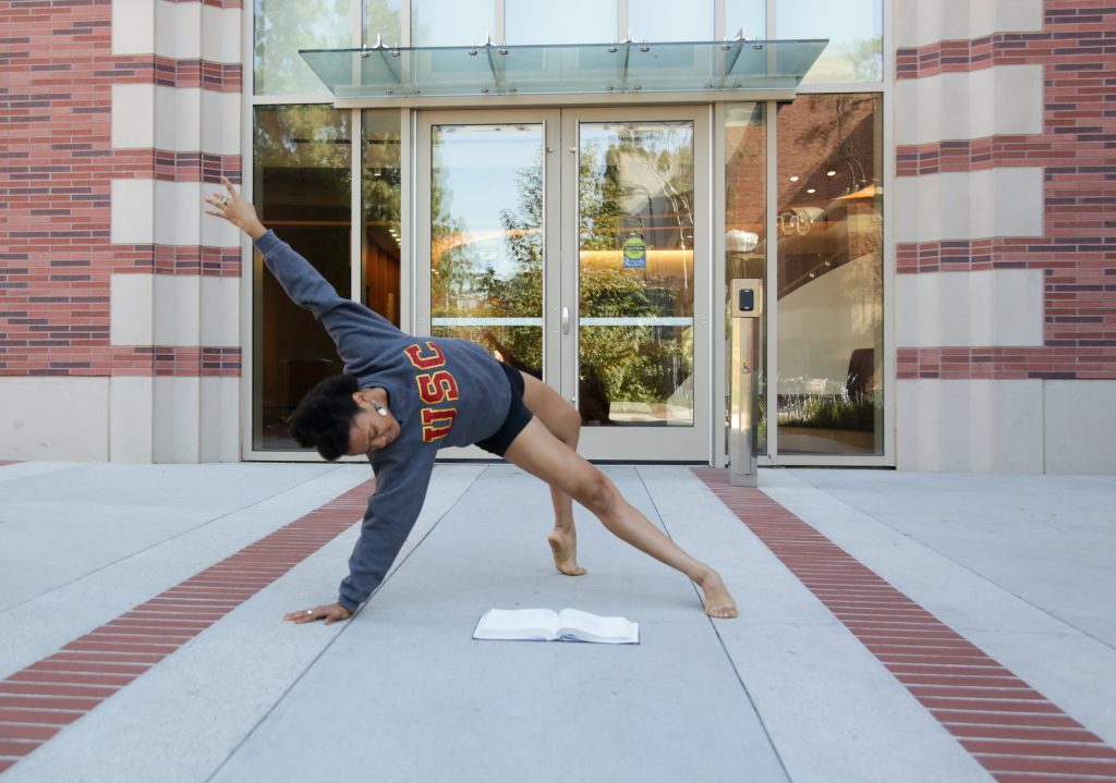 A female dancer strikes a pose as she reads a text book in front of the Glorya Kaufman Dance Center