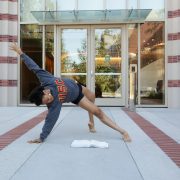 A female dancer strikes a pose as she reads a text book in front of the Glorya Kaufman Dance Center