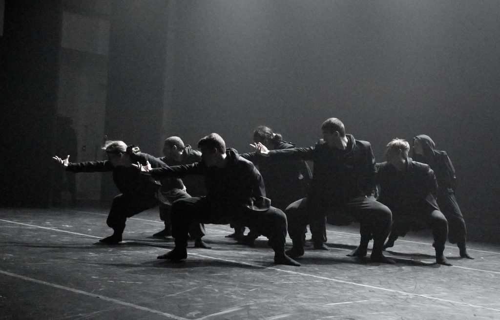 Dancers in all black on a dark stage.