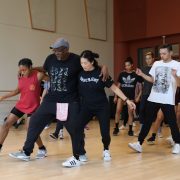 Teacher with his arms around two students as he teaches them dance steps in a studio.