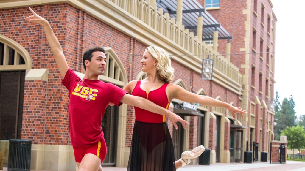 Man and woman in red and yellow dance attire outside at USC Village.