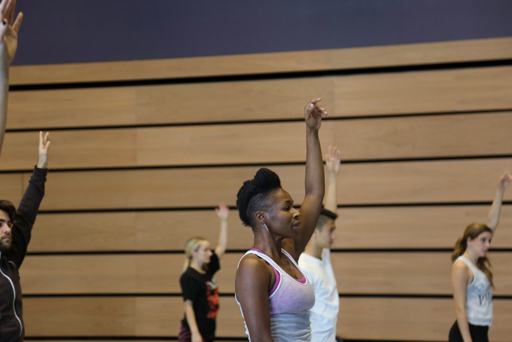 five dancers standing with their left arms lifted above their heads