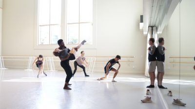 Dancers in a studio with choreographer at the front, directing.