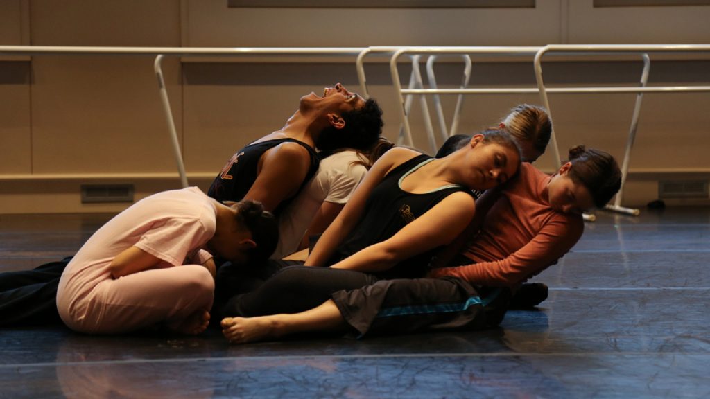 Dancers sitting in a clump and resting on each other