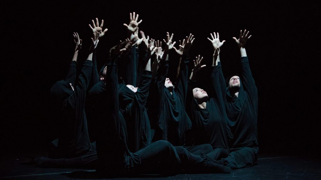 dancers wearing black sitting on the floor with both hands up in Aszure Barton's BUSK