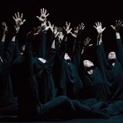 dancers wearing black sitting on the floor with both hands up in Aszure Barton's BUSK