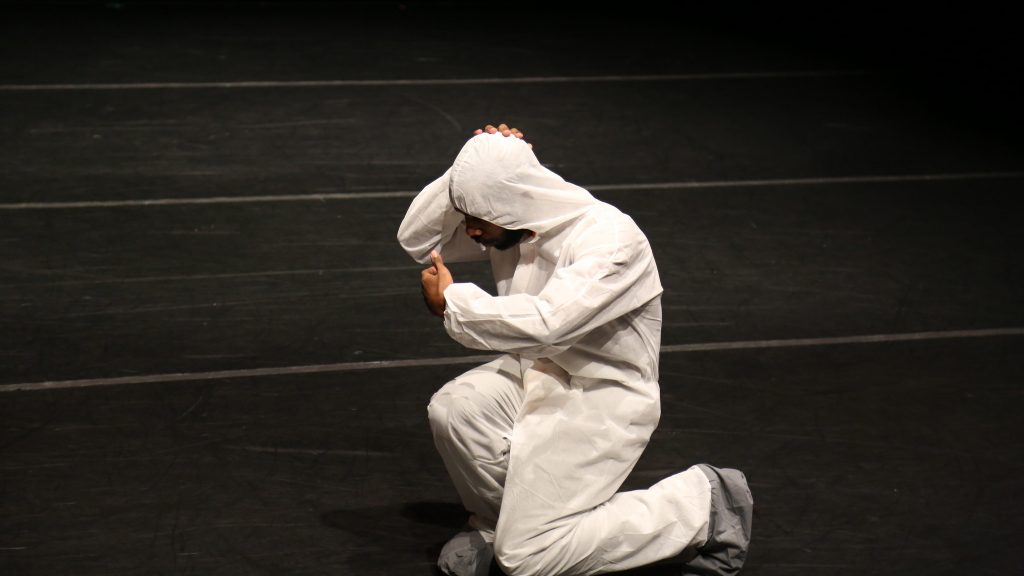 man kneeling in white hazmat suit