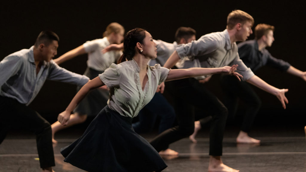 dancers in blue and gray clothing reaching forward on profile