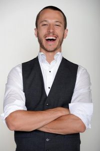 man with arms crossed and laughing wearing white button down and gray vest
