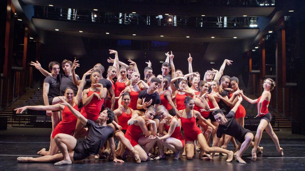 Many dancers in red and black posing onstage