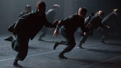 Dancers in all black running in a line onstage