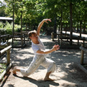 A boy dances in a park lined with trees and brown fences