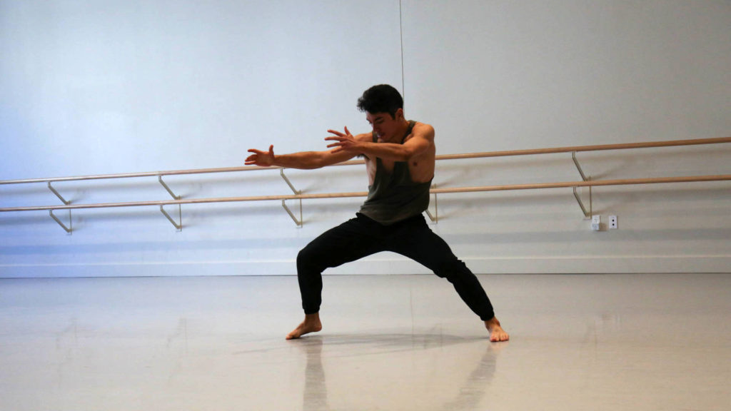 barefoot dancer wearing a green tank top and black pants with arms stretched out