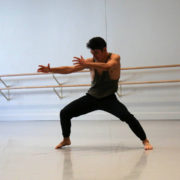 barefoot dancer wearing a green tank top and black pants with arms stretched out