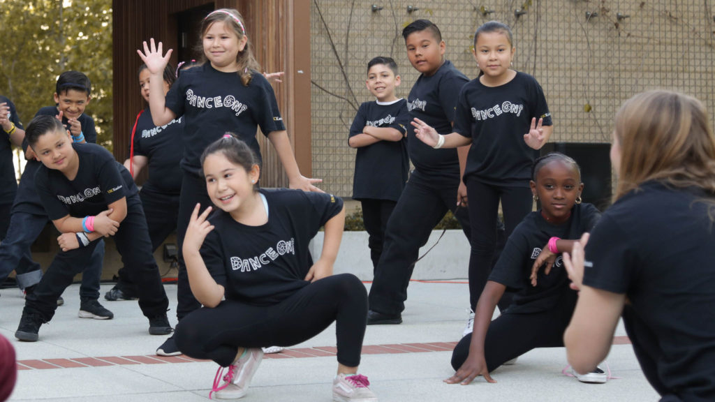 a group of of kids in black t-shirts that say "Dance On!" pose at the end of their performance