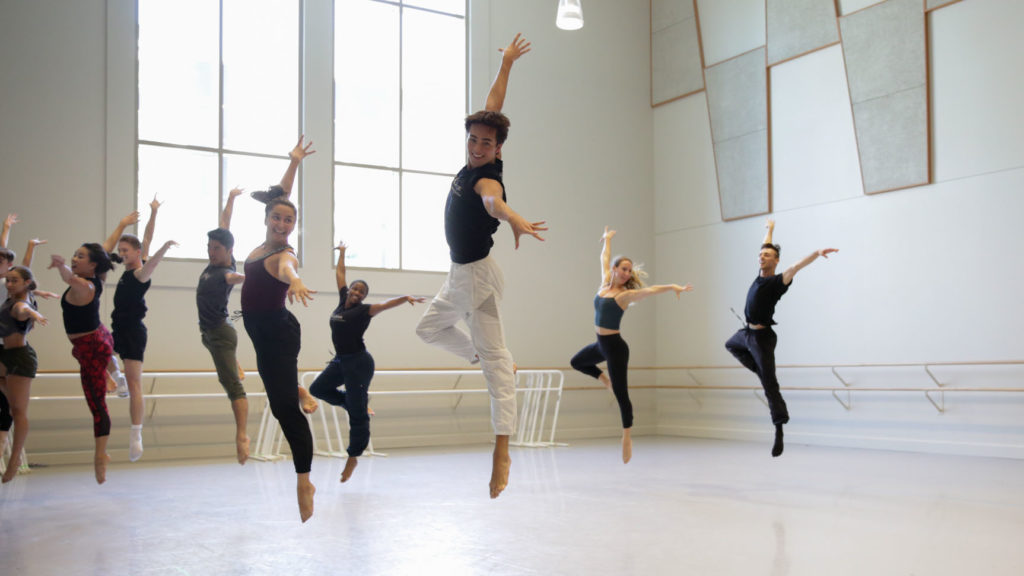 Zackery and a group of dance students jump in passe, with their arms extended to create a 90 degree angle