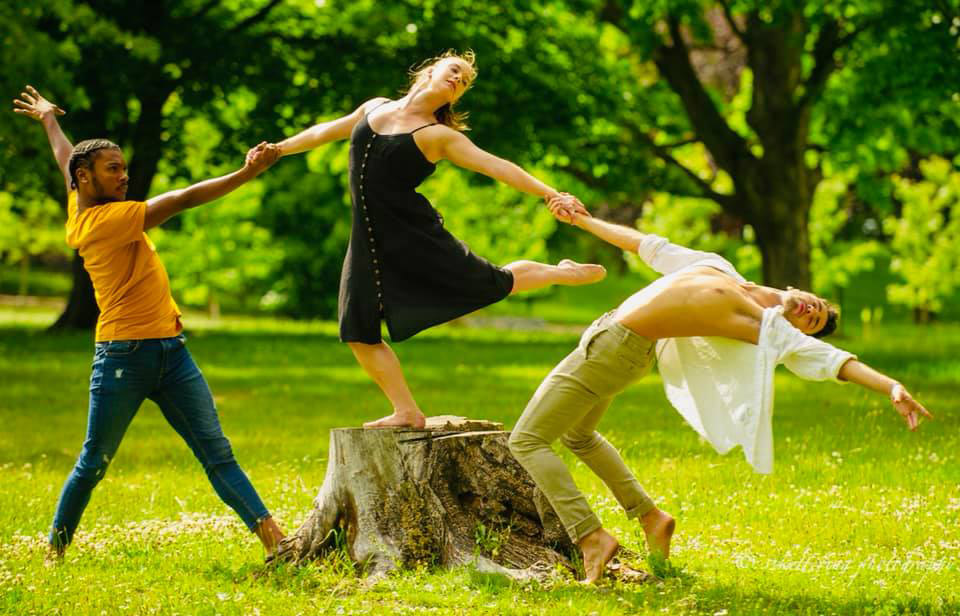 three dancers holding hands in a park
