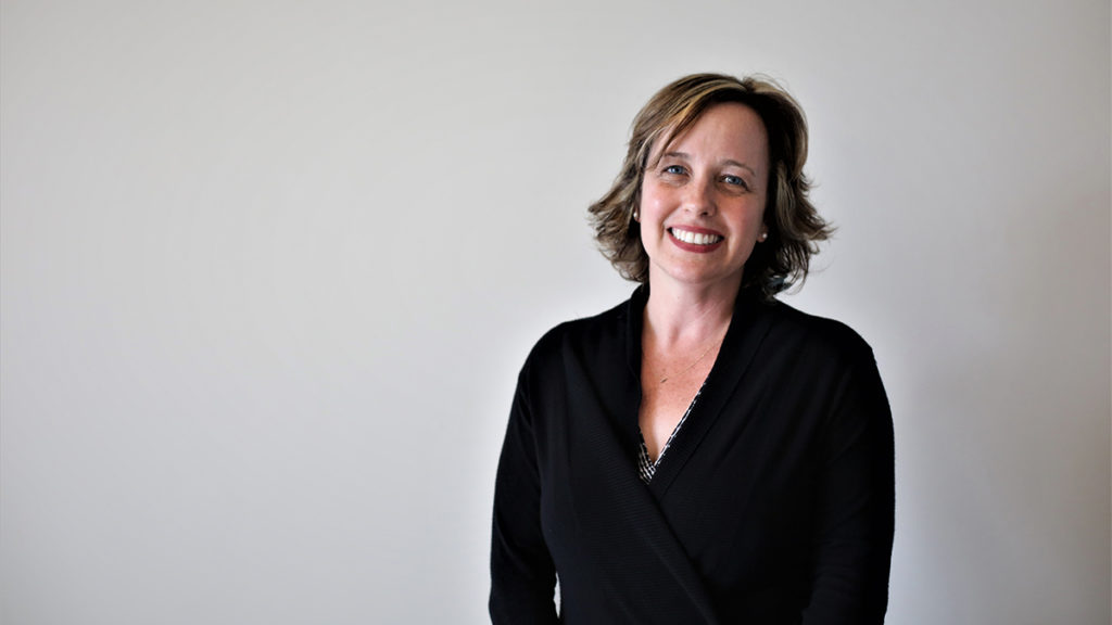 woman smiling wearing a black v-neck dress in front of a white wall