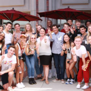 A group of USC Kaufman students pose around Deans Cutietta and Gates, all holding up a hand with their fingers in a "V" for victory