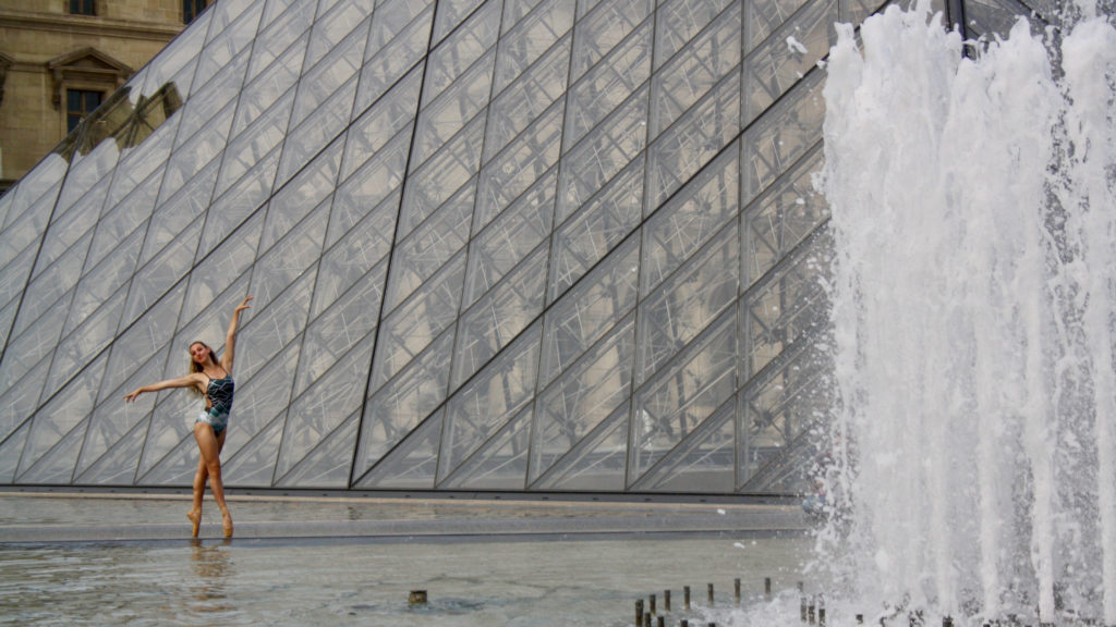 Isabella poses in fourth position en point by a fountain in front of the Louvre