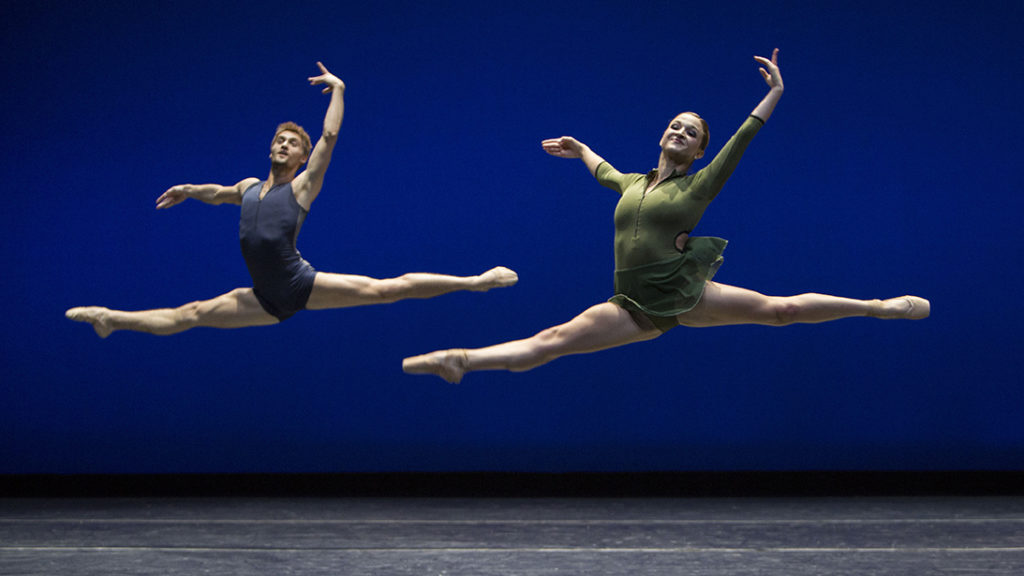 two dancers leaping against a blue backdrop