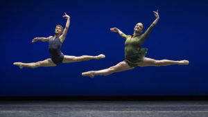 two dancers leaping against a blue backdrop