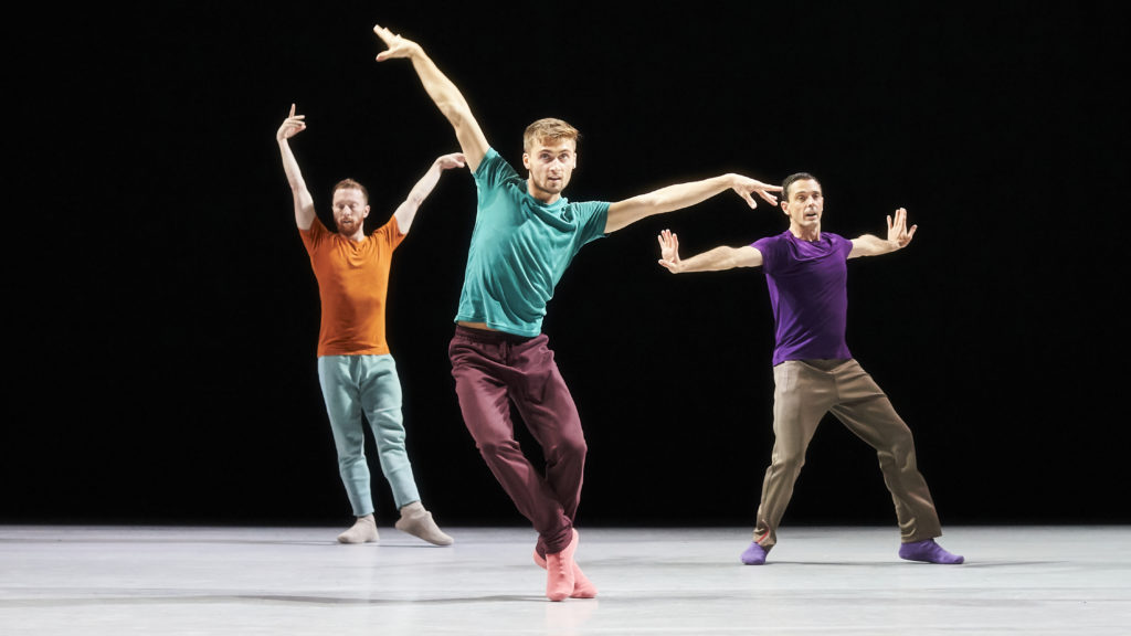 Three dancers in brightly colored t shirts and pants strike angular poses