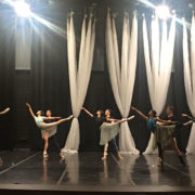 6 dancing couples pose in a partnered arabesque on a rehearsal stage