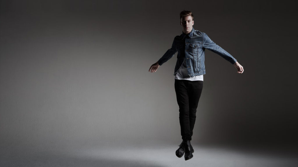 Andrew Winghart jumping in denim jacket and black pants