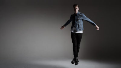 Andrew Winghart jumping in denim jacket and black pants