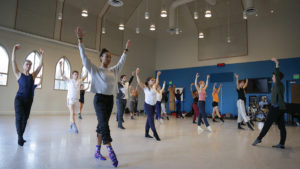 Dance students in their teacher stretch in a circle in a dance studio