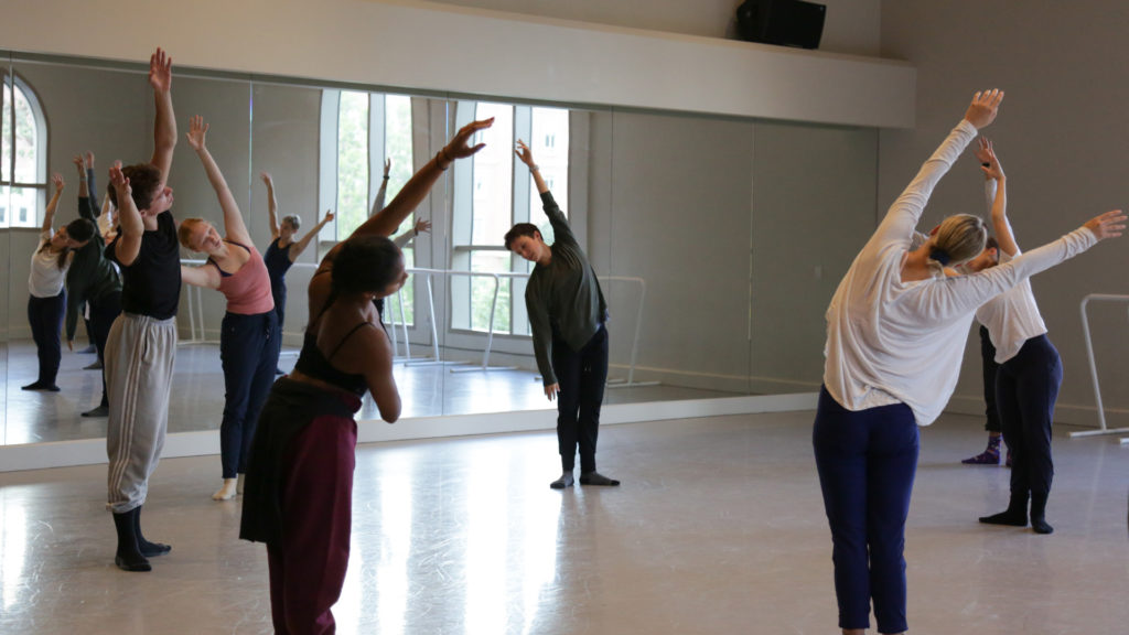 Dance students in their teacher stretch in a circle in a dance studio