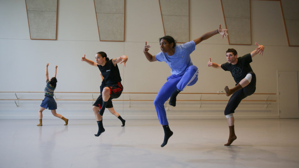 woman in all blue jumping with dancers behind her