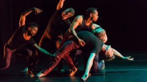 dancers wearing black tops and patterned pants perform on stage