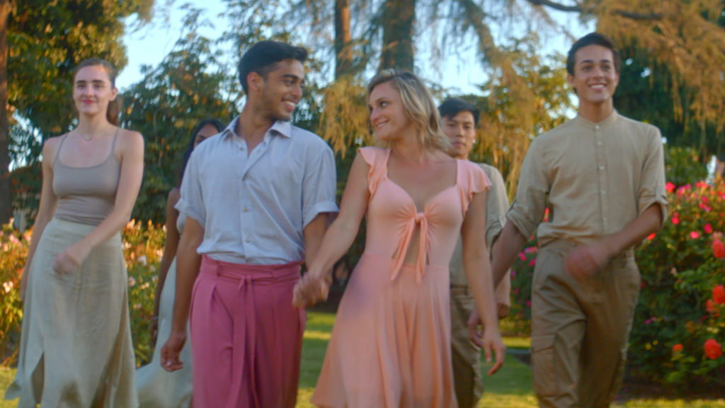 Two dancers hold hands and smile at each others as others walk behind them