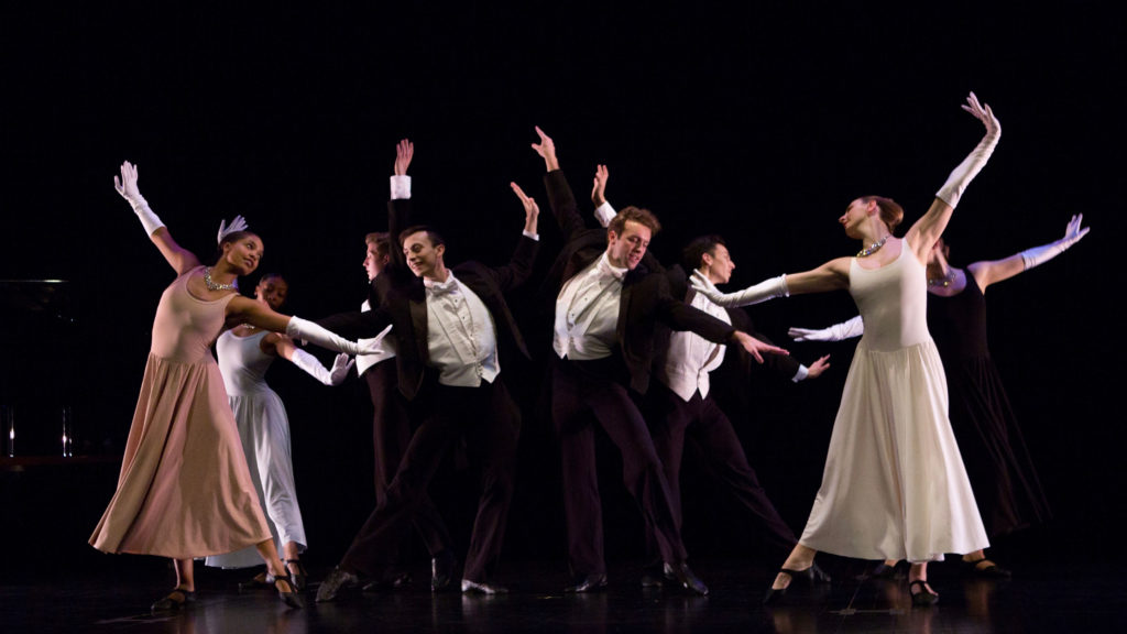 Dancers in formal attire perform in a group on stage