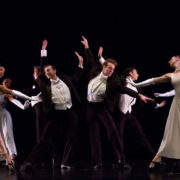 Dancers in formal attire perform in a group on stage
