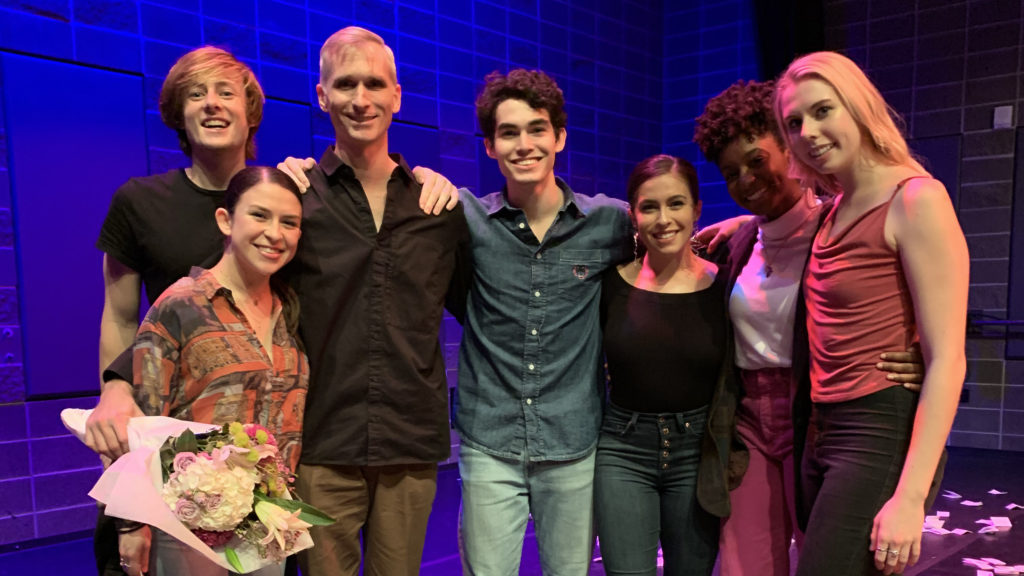 7 people smile together onstage after a performance