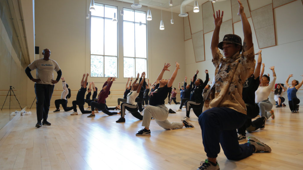 Fred Folkes stands at front of studio full of dancers