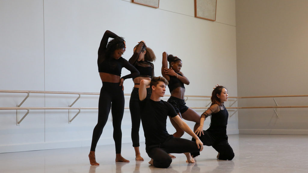 five dancers wearing black pose in a dance studio