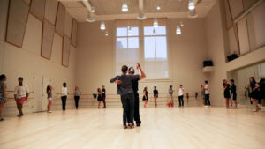 Jay Fuentes and partner demonstrate a ballroom move in the middle of a dance studio