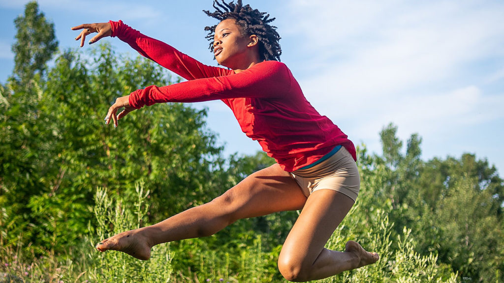 Rachel Harris jumping in front of green trees and blue skies