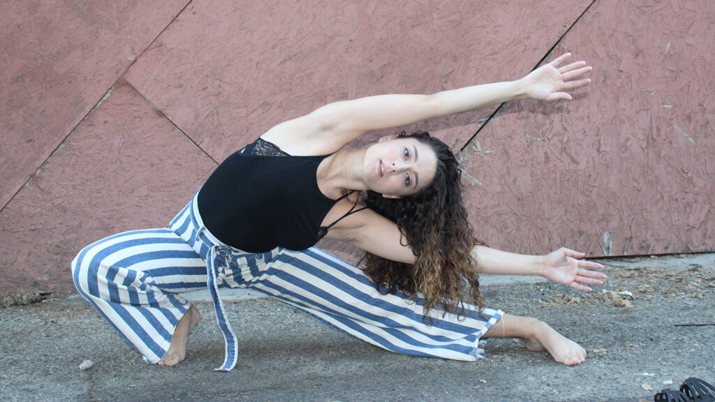 Aurora Vaughan lunging with arms stretched out to the side wearing a black tank and blue and white striped pants