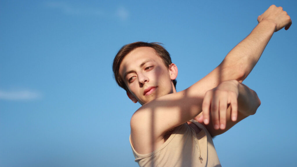 Cameron Cofrancesco looking over shoulder with arms raised in front of blue sky